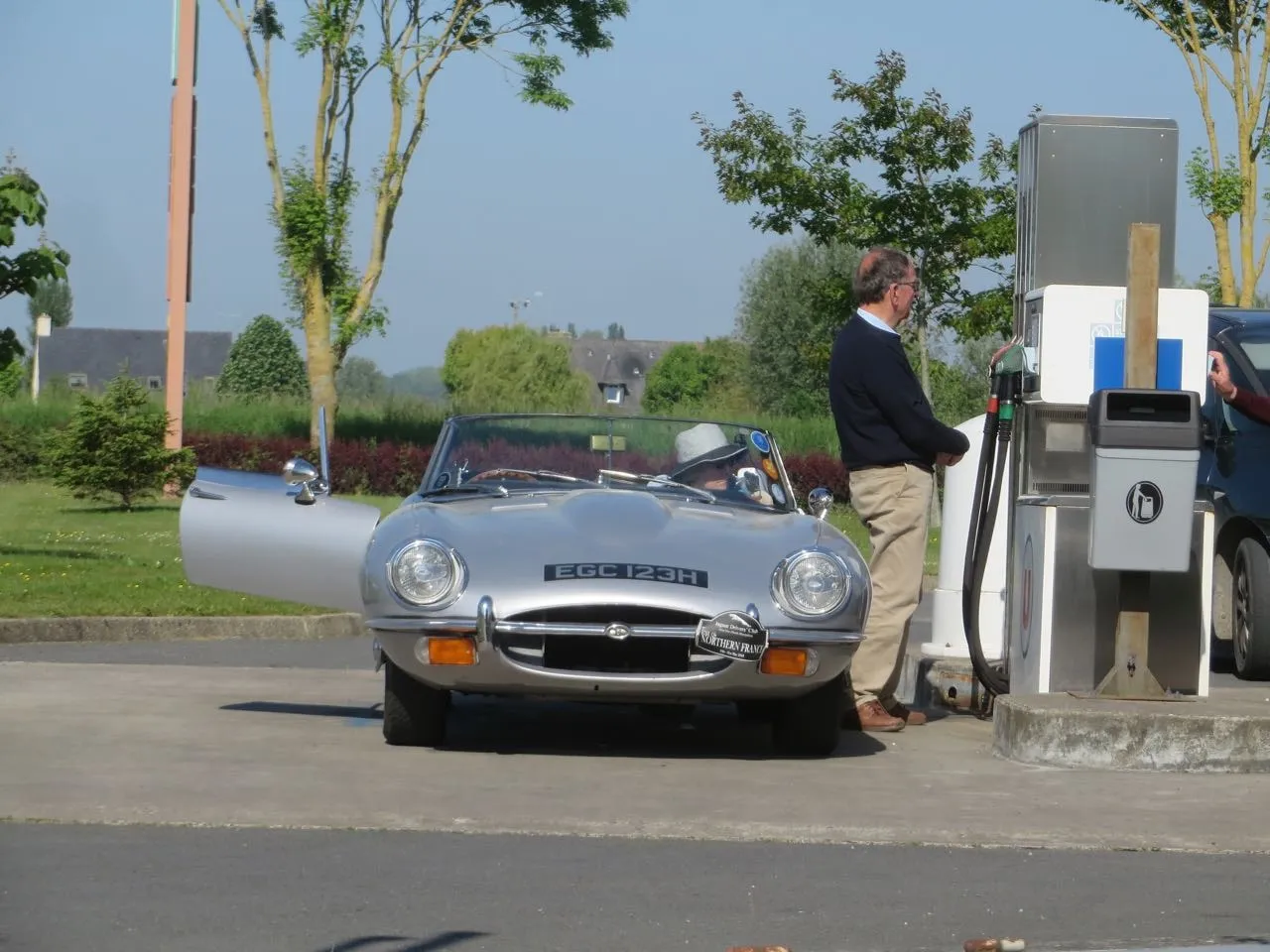A silver E-type stopped for fuel on a club tour of France